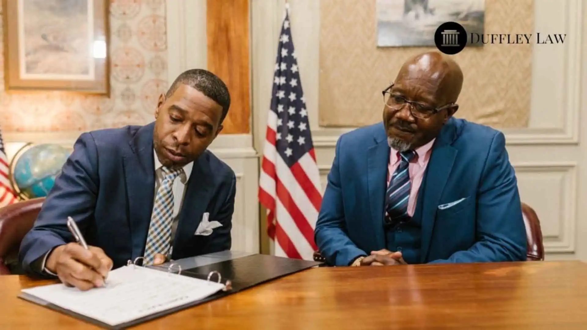 Two businessmen in suits sitting at a table signing documents in a formal office setting, illustrating trust attorney in Kady. Branded with the Duffley Law logo.